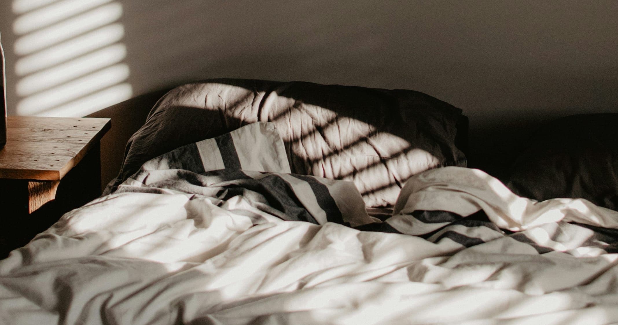 Obäddad säng i morgonljus.