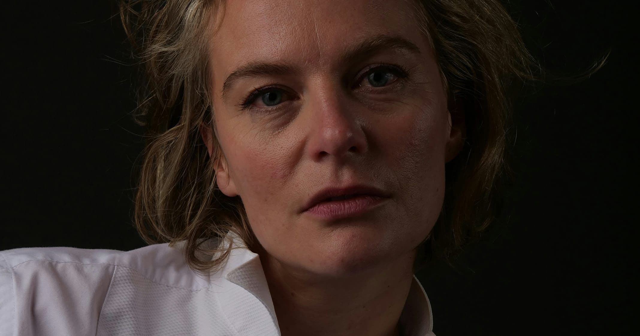 Porträtt av en allvarlig kvinna mot mörk bakgrund.