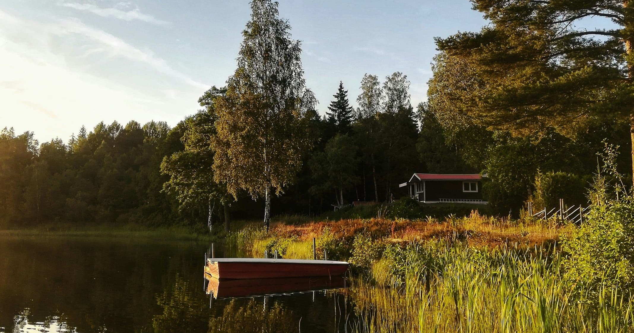En brygga i en sjö vid en skog med en röd stuga.